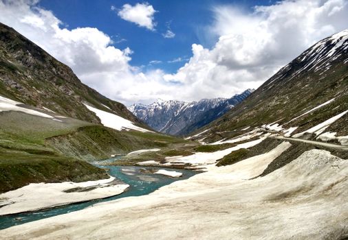 Breathtaking view of a river winding through a snow-capped Himalayan valley under a bright blue sky.
