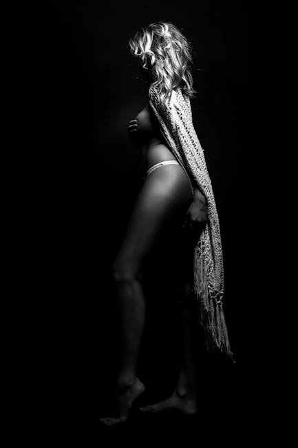 Monochrome studio portrait of a woman gracefully posing with a shawl, creating a dramatic and elegant silhouette.