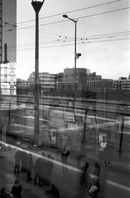 Black and white image of an urban railway station with reflections and people.