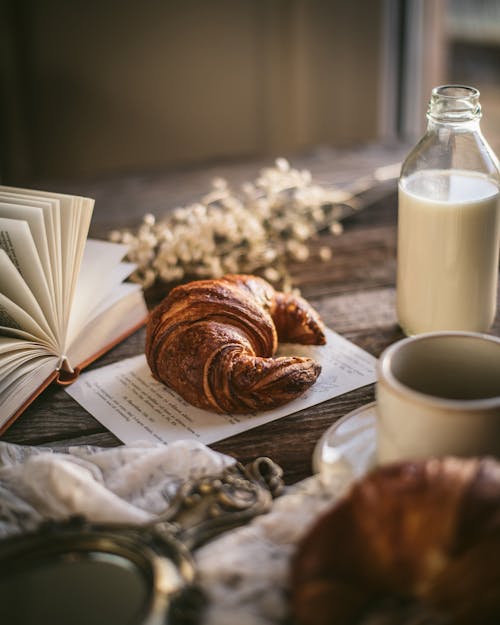 Croissant and Milk Bottle Next to Open Book