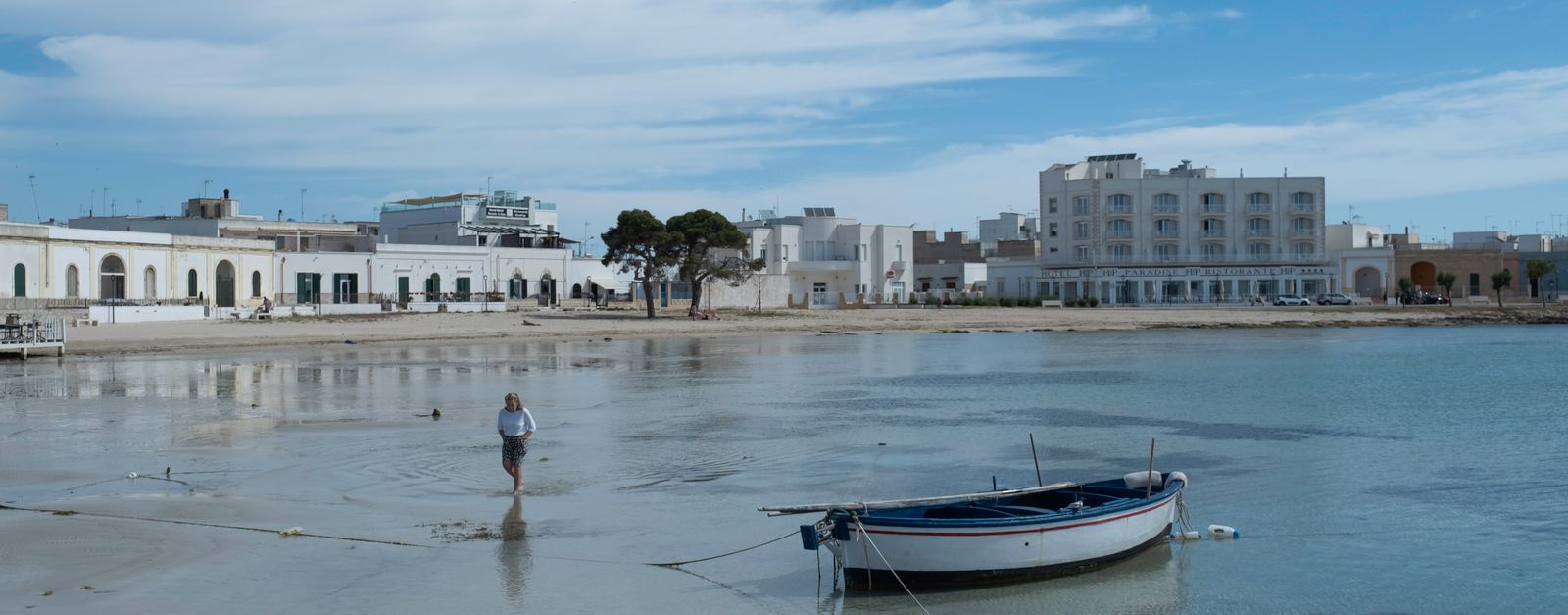Peaceful seaside view with a moored boat and coastal buildings in Salento, Italy.