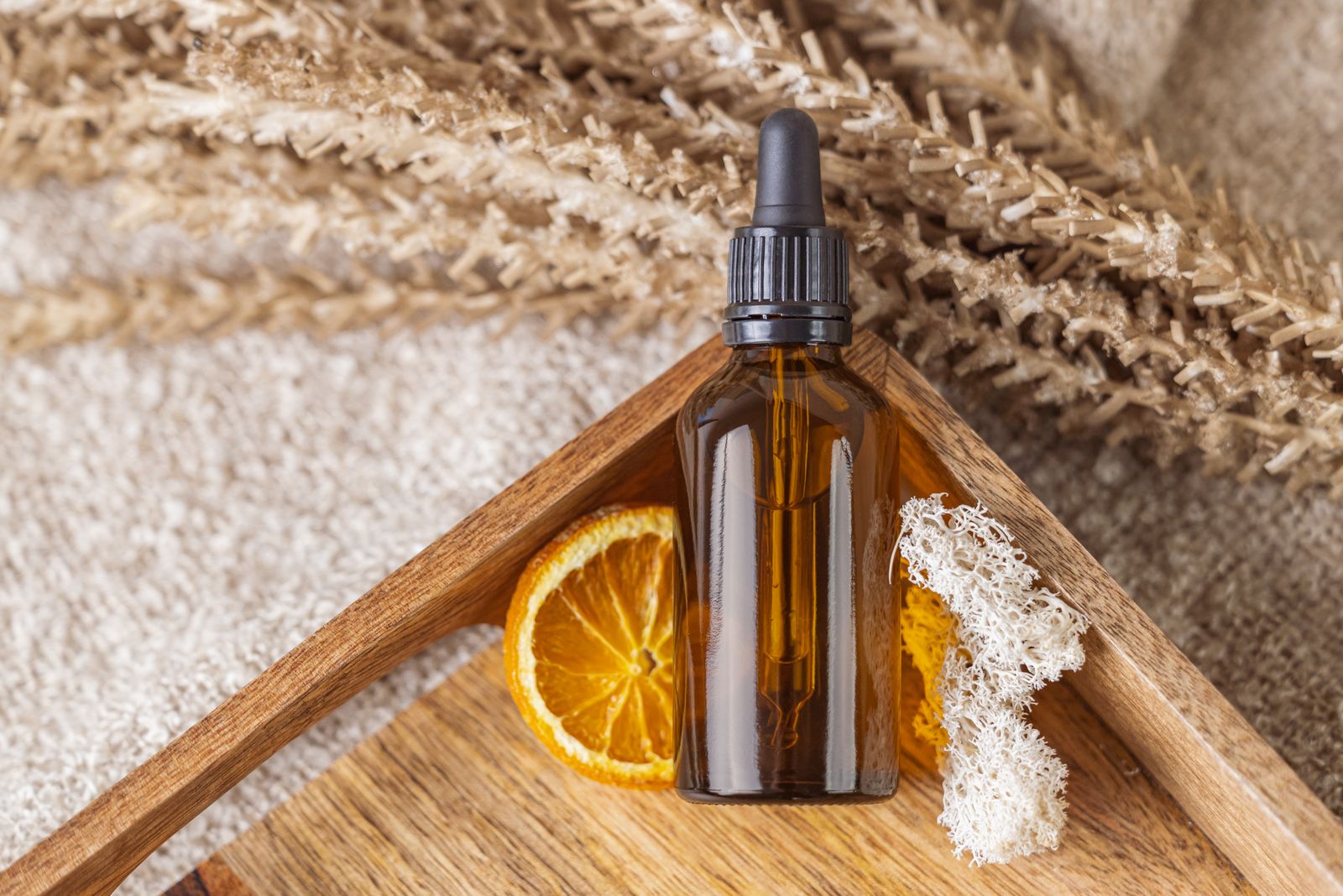 Amber glass dropper bottle on a wooden tray with a dried orange slice, moss, and dried grasses