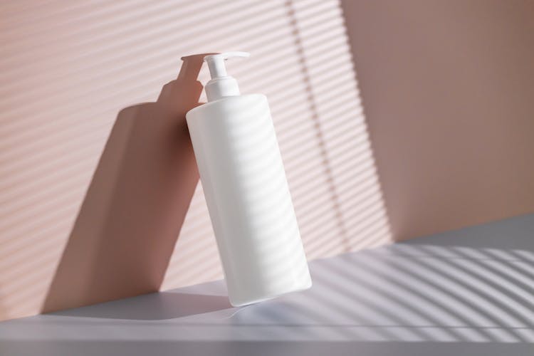 White Body Balm Bottle With Pump Leaning Against Pink Wall