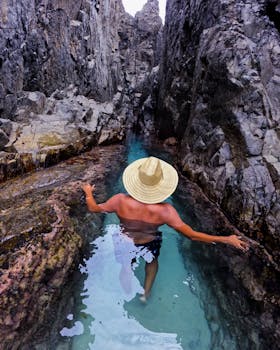 A shirtless man in a straw hat explores a narrow rocky passage in PE, Brazil.