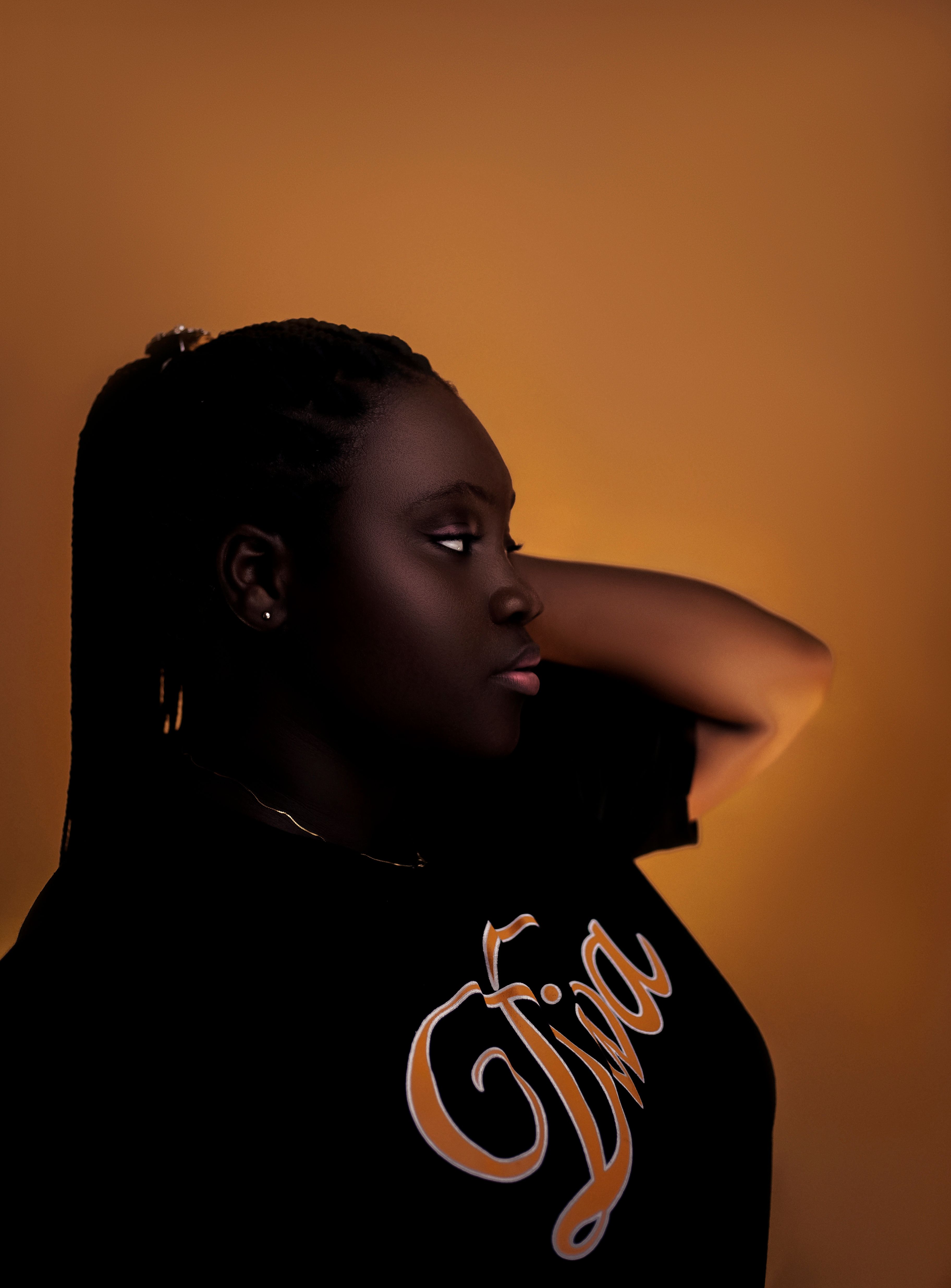 Side view portrait of a woman in a black t-shirt with script, against a warm background.