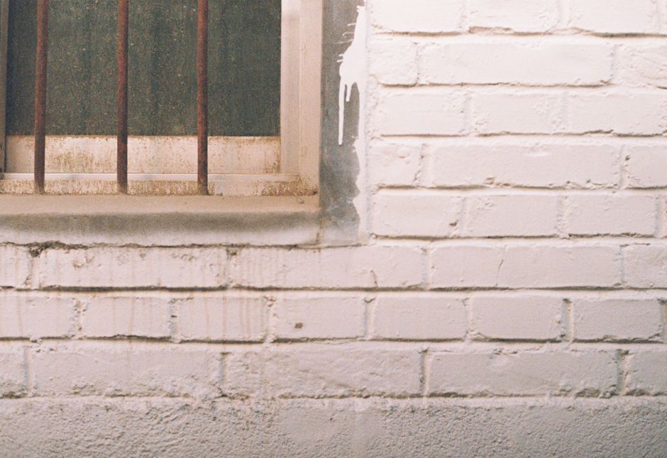 White painted brick wall showing salt efflorescence and damp staining beneath a barred window