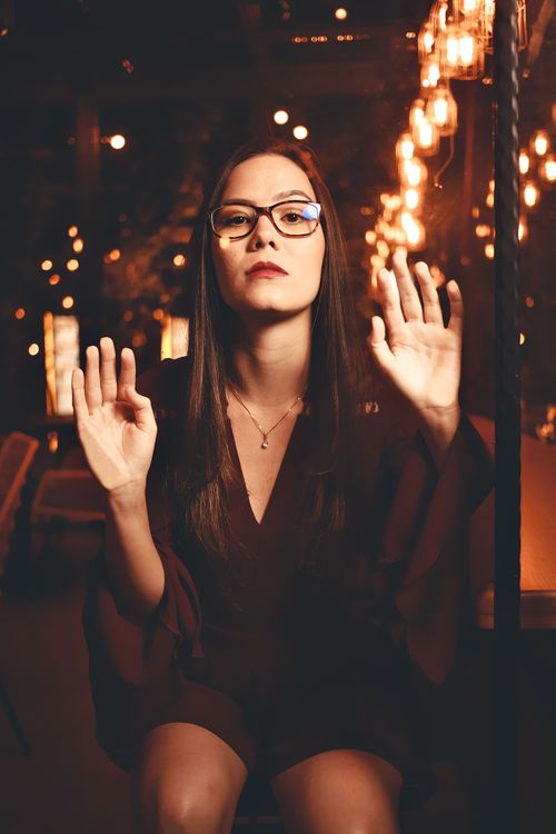 Free A woman wearing glasses poses behind glass with moody lighting, creating a dramatic scene. Stock Photo