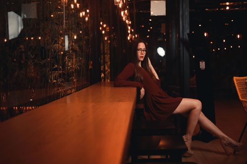 Free Stylish woman in red dress sitting indoors at night with moody lighting. Stock Photo