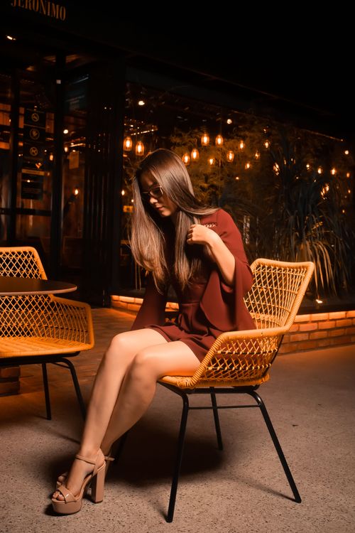 Free Asian woman in maroon dress sitting at a cafe with moody lighting, showing elegance and style. Stock Photo