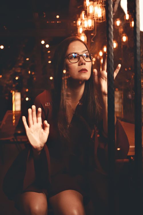 Free Thoughtful woman behind glass with warm night lights. Stock Photo