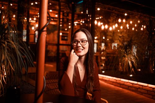 Free A young woman with glasses smiles warmly in a cozy indoor setting with ambient lighting. Stock Photo