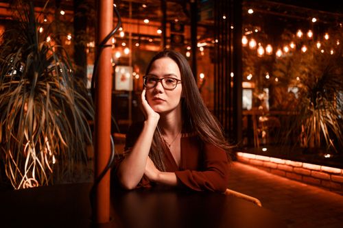 Free Asian woman wearing glasses, posing at a cozy cafe table. Warm, ambient lighting. Stock Photo