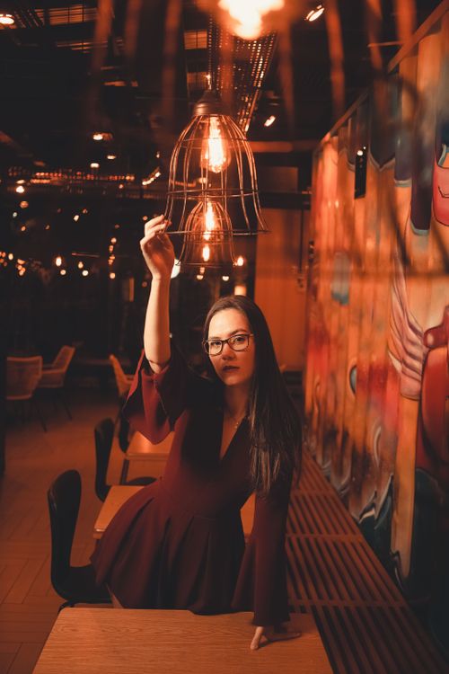 Free Young woman in a maroon dress poses under artistic indoor lighting. Stock Photo