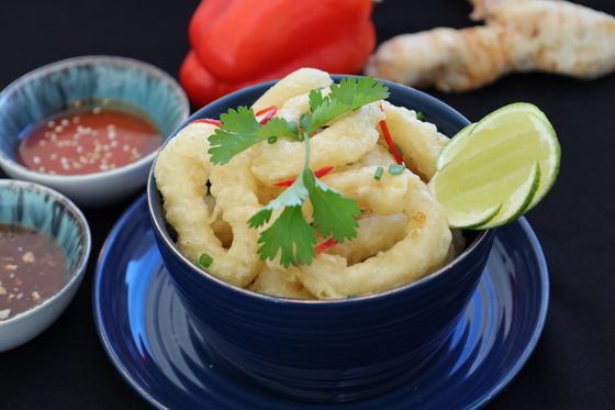 Blue bowl of pale tempura squid rings with cilantro, red chili, lime wedge and dipping sauces
