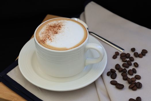 A cozy composition of a cappuccino cup with sprinkled cinnamon and scattered coffee beans on the side.