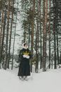 Woman in Black Dress Standing on Snow Covered Ground Surrounded by Trees