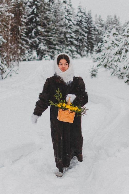 Woman Holding a Basket While Walking on Snow Covered Ground