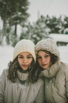 Two women bundled up in hats and jackets enjoying a snowy day outdoors.