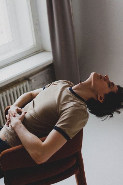 A person sits comfortably on a chair, leaning back with hands together in a contemplative pose.