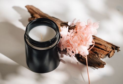 Free A close-up of a black candle with delicate pink flowers and rustic wood, evoking a serene ambiance. Stock Photo