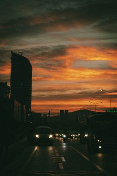 City street scene at sunset with buildings, cars, and vibrant red sky.