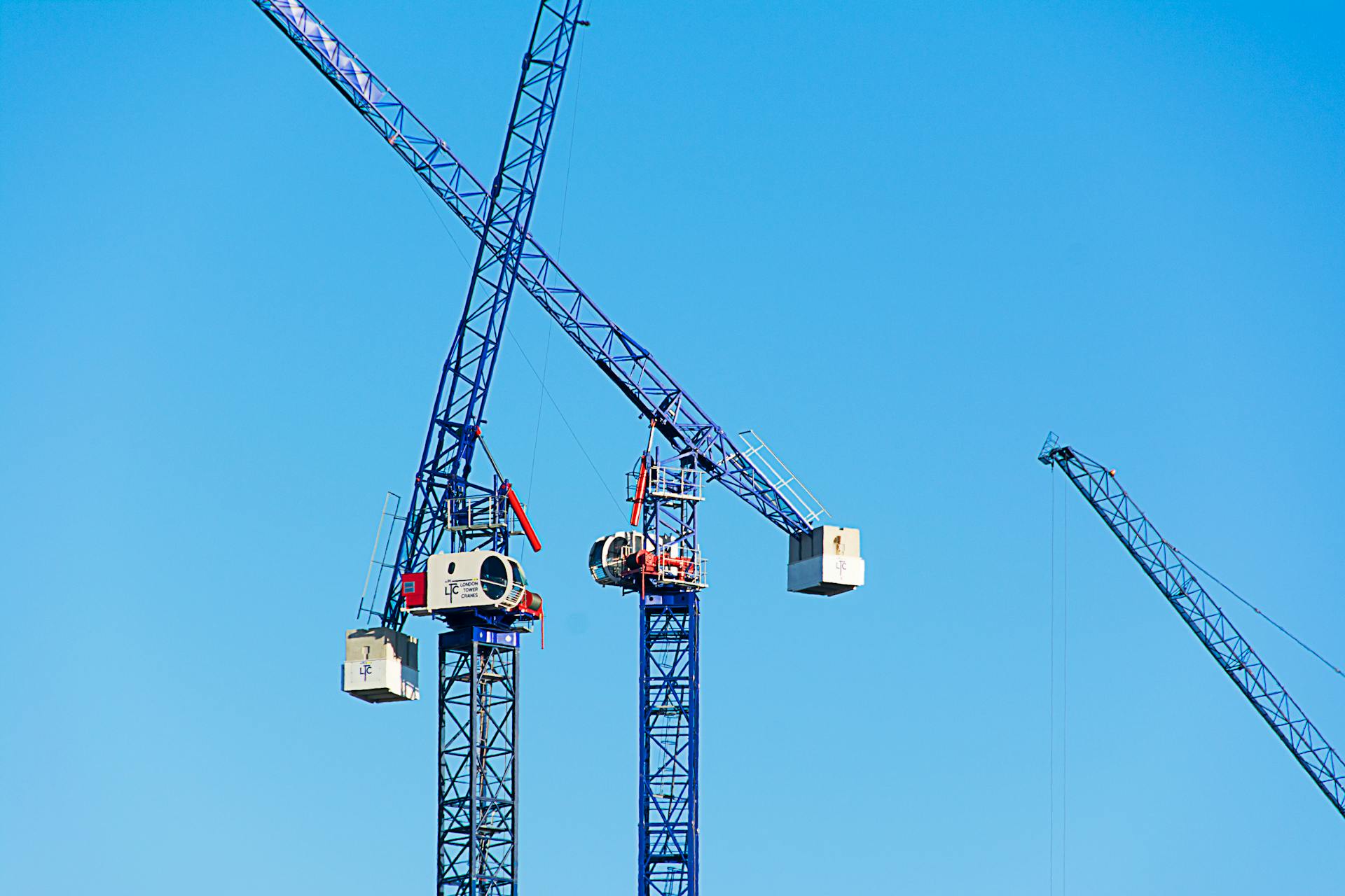 High vantage view of modern tower cranes operating under a clear blue sky on a construction site.