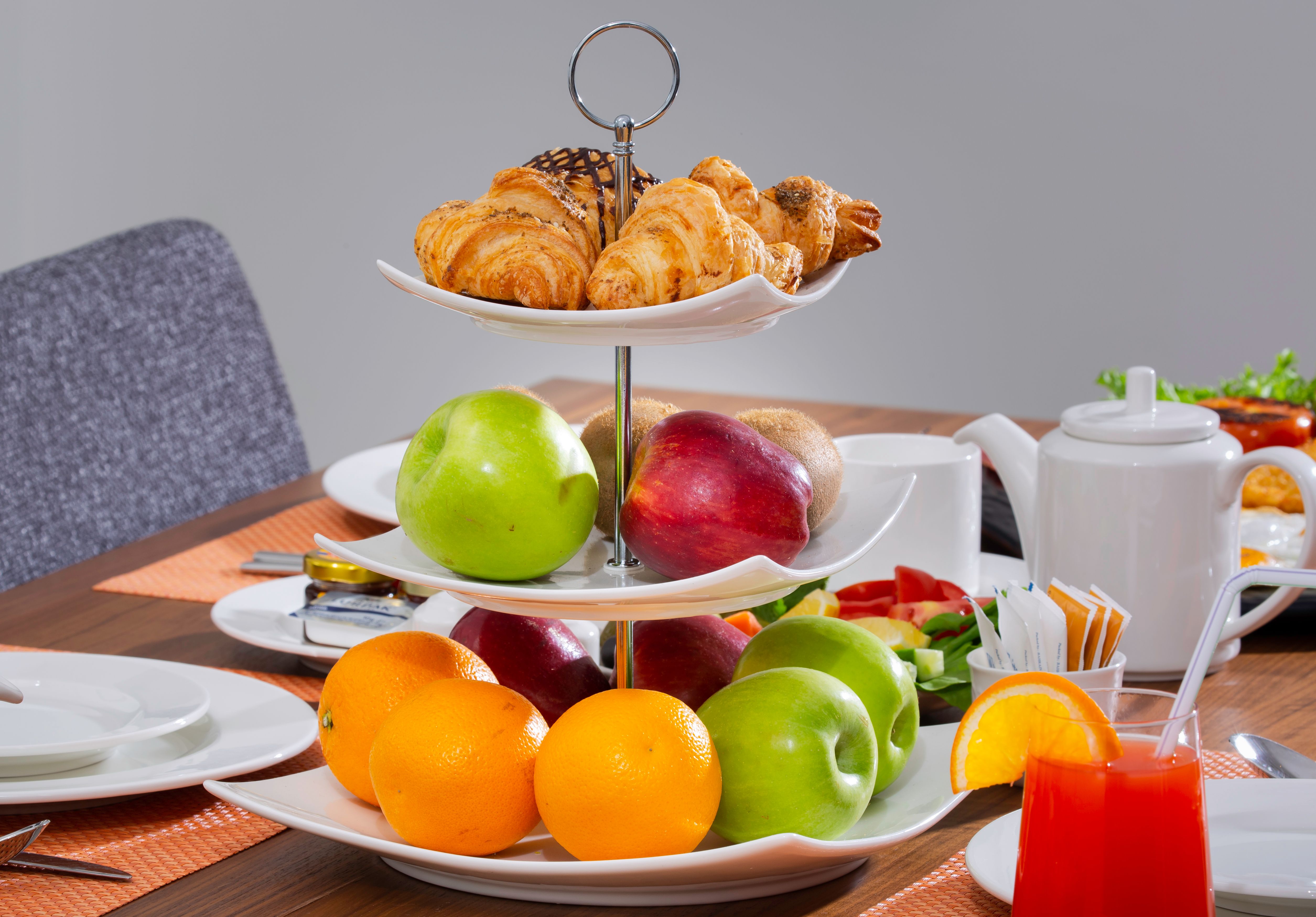 A three-tiered platter with fresh croissants and fruits on a breakfast table. Bright and appealing.