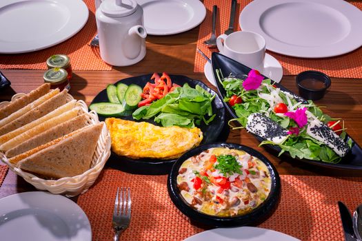 Colorful breakfast platter featuring omelette, salad, fresh veggies, and assorted bread.
