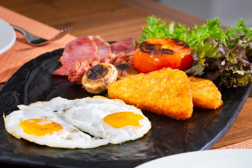 Free Gourmet breakfast plate featuring fried eggs, bacon, hash browns, and fresh vegetables. Stock Photo
