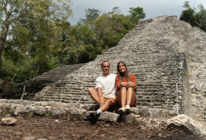 A happy couple sitting in front of ancient Mayan ruins surrounded by nature.