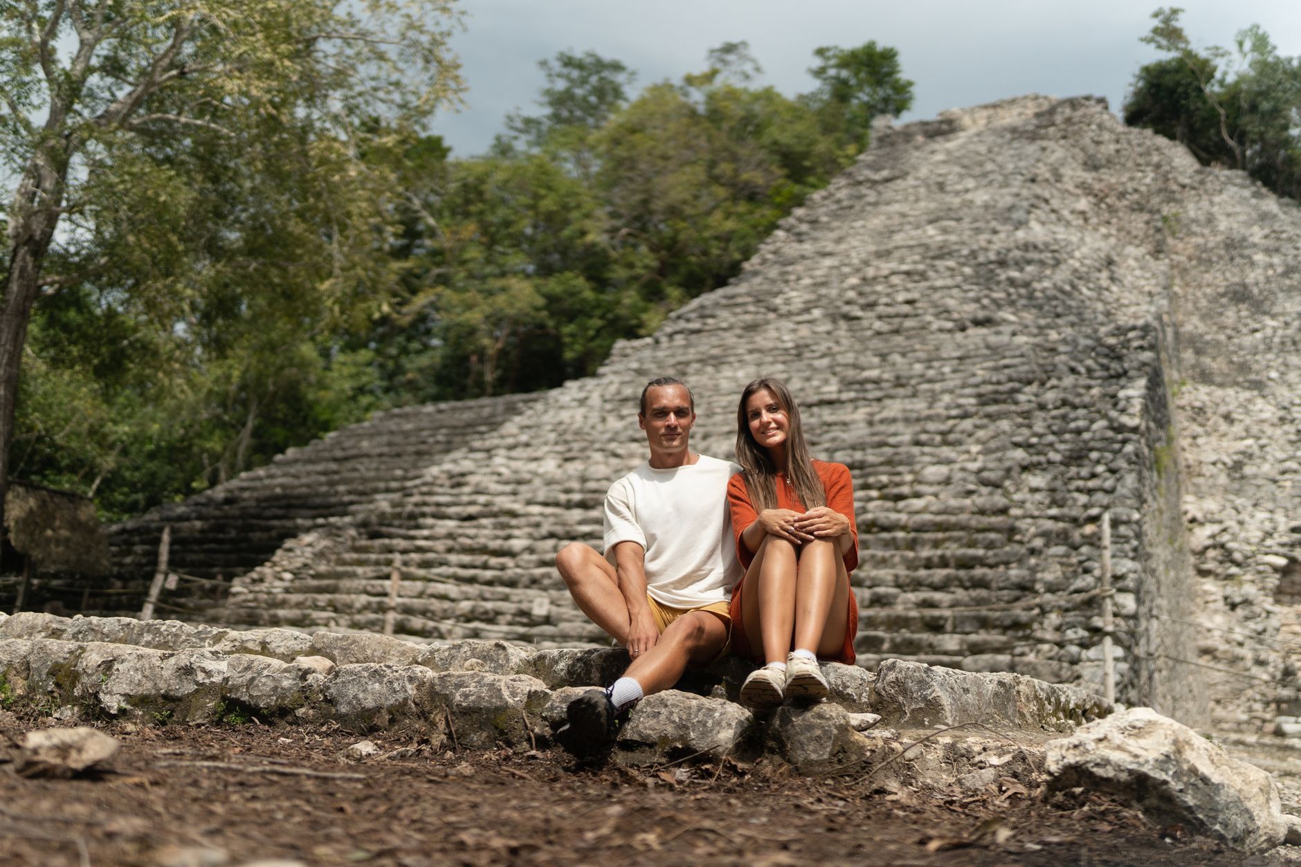 A happy couple sitting in front of ancient Mayan ruins surrounded by nature.