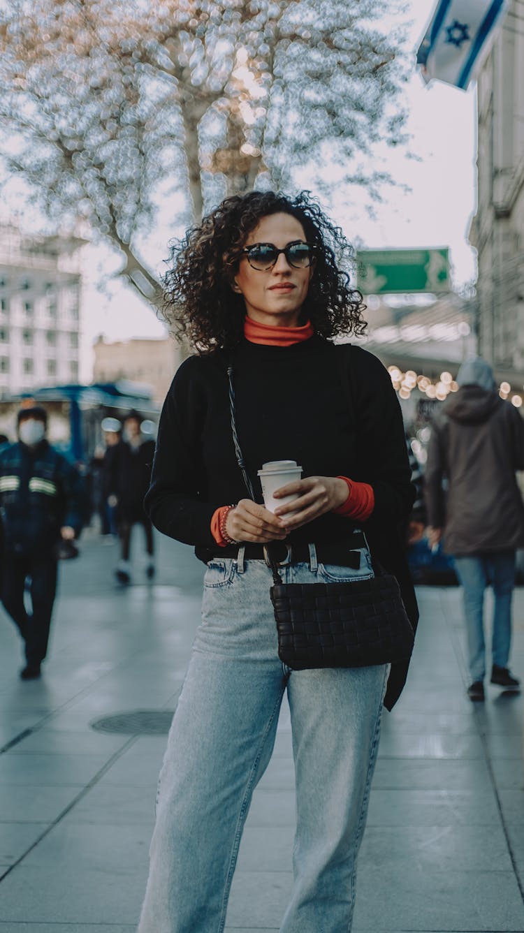 A Woman Standing On A Busy Street Holding A Coffee Cup