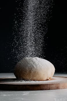 Captivating image of dough on a board as flour gracefully falls, highlighting baking creativity.