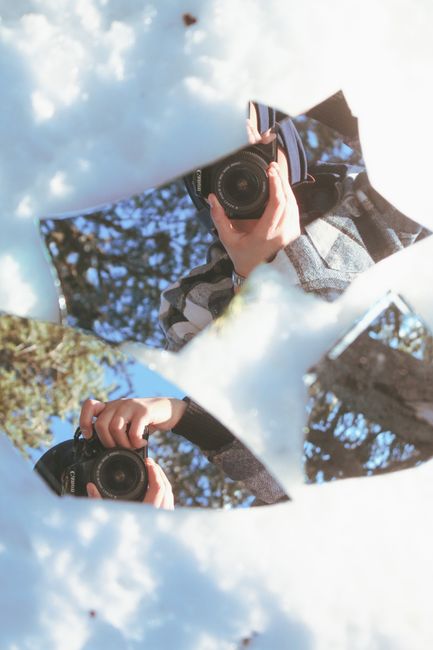 A camera captures a reflective self-portrait using a shattered mirror amidst snow outdoors.