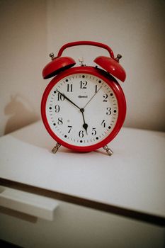 Vintage red alarm clock with white face and black numerals on a white surface.