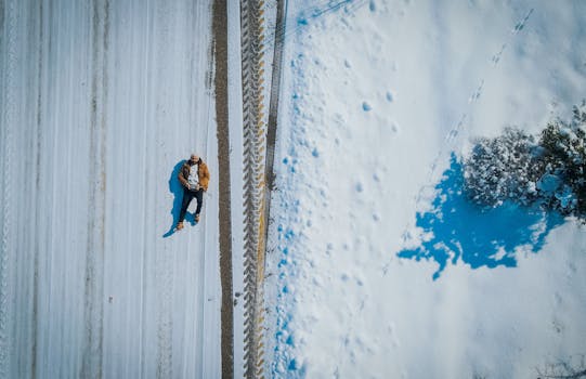 Drone shot of a man lying on a snow-covered road with visible tire tracks during winter.