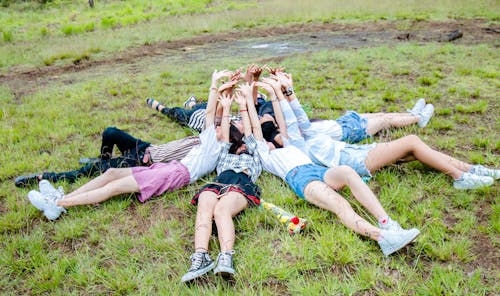 Free Group of Friends Form in Circle While Lying on the Grass While Hands on Top Stock Photo