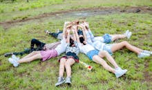 年轻的成年人躺在草地上，围成一个圈，举起手臂，表达着户外的快乐和友谊