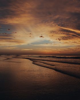 A breathtaking sunset casting warm hues over the calm ocean waves, creating a tranquil beach scene.