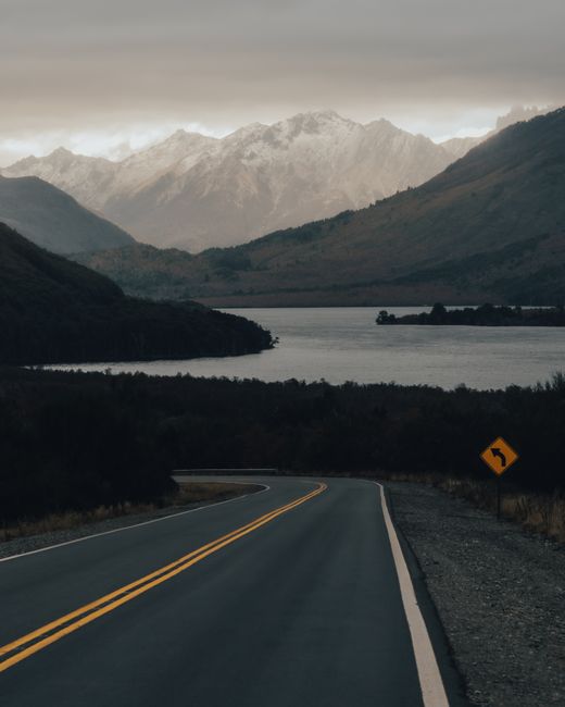 A winding road leads to mountains beside a tranquil lake, capturing serene natural beauty.