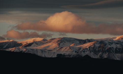 Free Serene snowy mountains illuminated by sunset with dramatic clouds overhead. Stock Photo