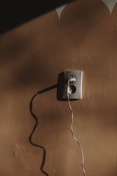 A plug and cord in a wall socket on a warm-toned wall