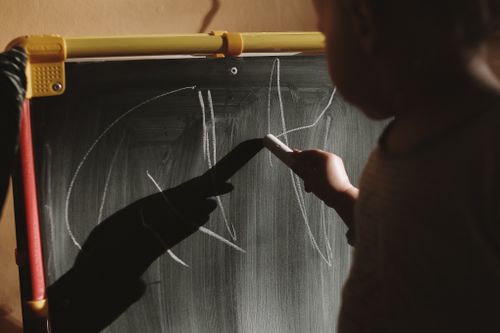 Free Close-up of a child using chalk on a blackboard in warm lighting. Stock Photo