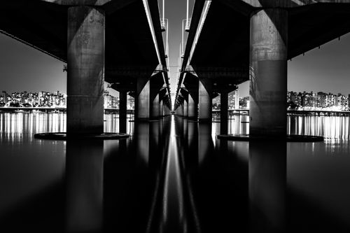 Free Black and white photograph of a bridge in Seoul with city lights reflecting in the river at night. Stock Photo