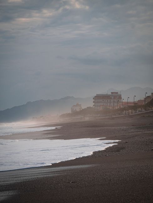 A misty seaside view with distant buildings and mountains during twilight.