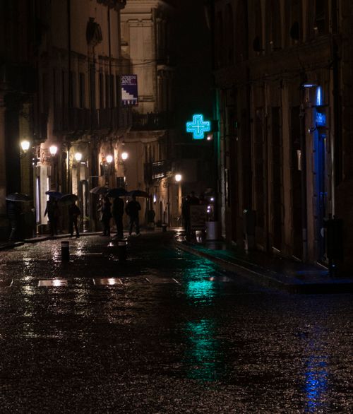 Free A rainy urban street scene at night, featuring silhouetted pedestrians and vibrant reflections on the wet pavement. Stock Photo