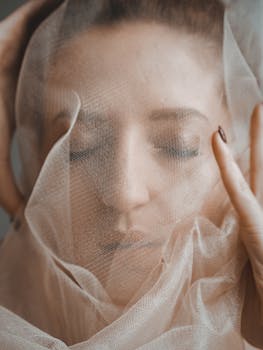 Elegant and serene portrait of a woman with closed eyes wrapped in sheer veil.