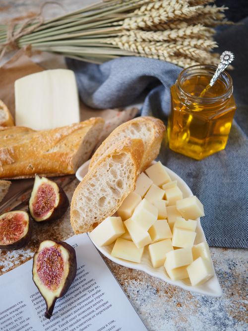 Free Artistic flat lay of baguette, cheese cubes, figs, and honey for a delightful rustic breakfast scene. Stock Photo