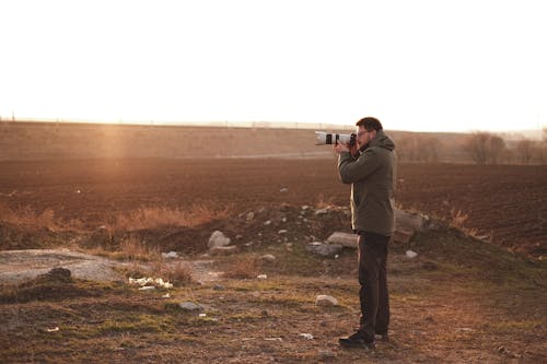A Man Standing in a Field While Taking Photo with a Camera