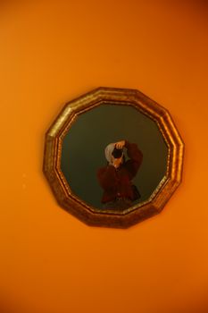 Person reflected in an octagonal mirror on a vibrant orange wall, capturing a photo.